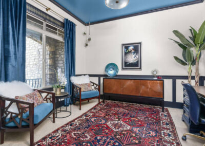Interior Design of office inspired by artwork Blue chairs, black and wood credenza, red and blue rug, blue drapes large banana plant