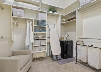 stocked closet with towels, robes and linens, plus chair and ironing board showcases elegant interior design for guest bedroom closet